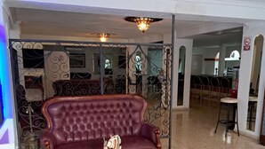 Una sala de estar con un sofá de cuero marrón oscuro, un reposapiés a juego y una mesita con un objeto decorativo. El cuarto tiene piso de baldosas y una partición metálica con diseños intrincados.