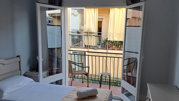 Habitación de hotel con dos camas, un balcón con vistas y una pequeña mesa.