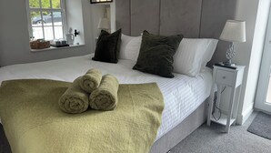 Una cama bien hecha con toallas enrolladas, una mesita de noche con una lámpara, y una ventana con vistas al exterior.