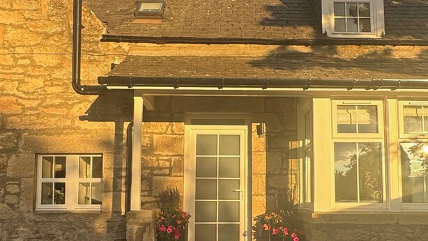 Una casa de piedra con porche delantero, chimenea y una ventana con puerta.