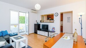 Ett modernt vardagsrum med en soffa, ett soffbord och ett matbord. Här finns också en tv, ett köksområde och ett stort fönster.