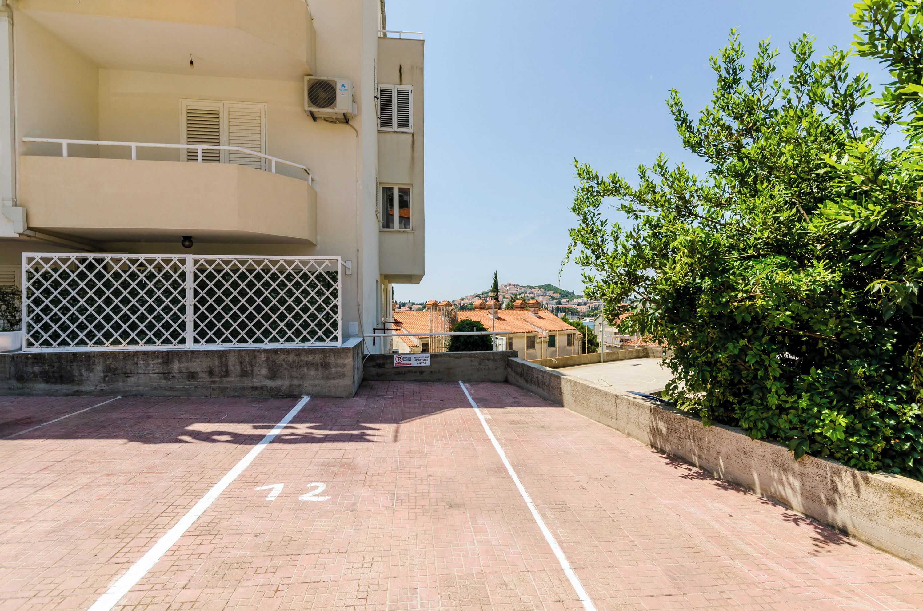 A parking area with a building in the background, a tree, and a clear sky.