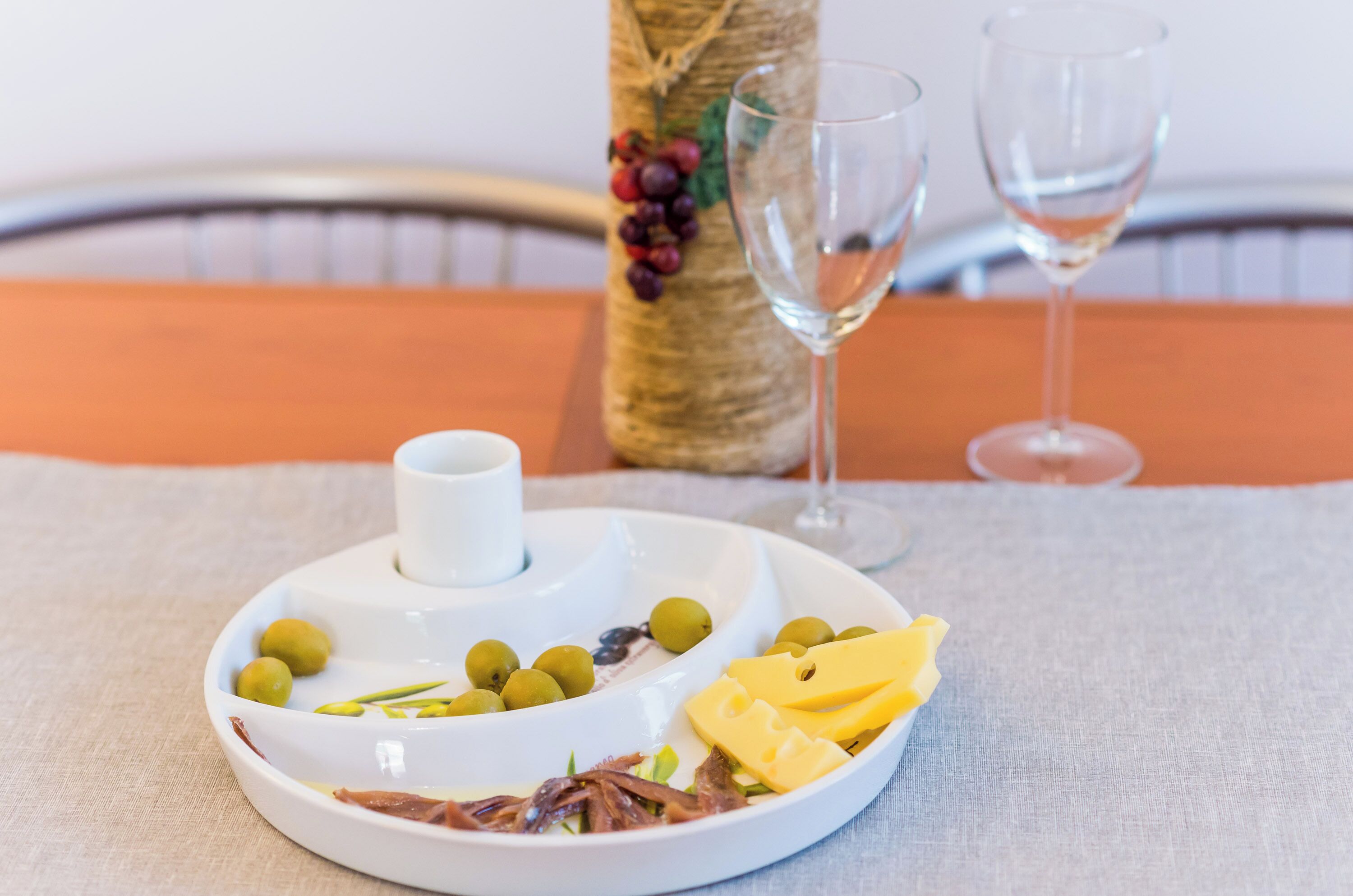 A white serving tray with olives, cheese, and greens on a tablecloth.
