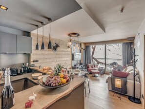 A modern kitchen with a wooden countertop, a fruit bowl, and a dining area with a sofa and a chair.