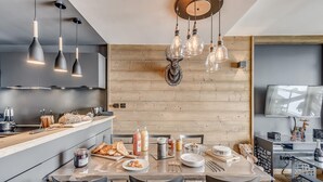 A modern kitchen with a wooden accent wall, a dining table set for four, and a ceiling light fixture. - 4* Apartment Tignes 2 rooms, 4 people (Tignes)