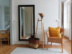 A room with a large mirror, a wicker chair with a yellow pillow, a wooden ladder, and a wicker basket on a white rug. - Charming Village Home with Garden, Terrace, BBQ, Billards & Near Nature Park (Crucey-Villages)