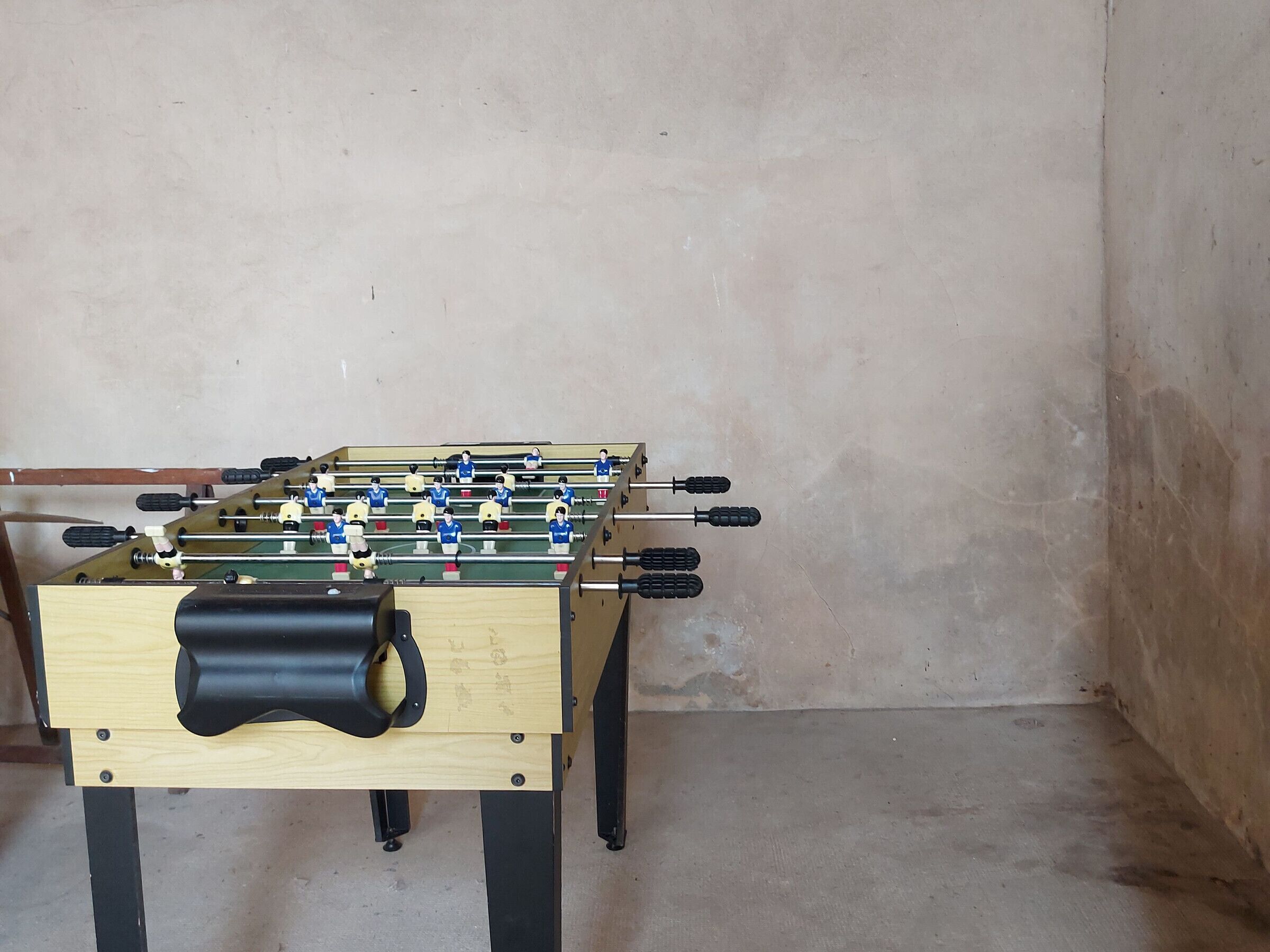 A foosball table with a wooden base and metal legs, set against a plain wall.
