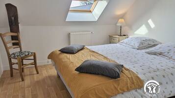 Une chambre avec un puits de lumière, une chaise en bois, une table de chevet avec une lampe et un lit avec une literie à motifs floraux.