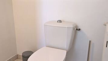 A standard white toilet with a tank, a small trash bin, and a toilet brush.