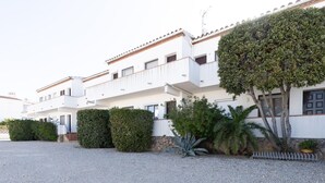 A multi-story building with balconies, a gravel driveway, and various plants.