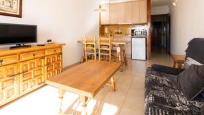 A living room with a TV, wooden furniture, a sofa, and a kitchen area with cabinets and appliances.
