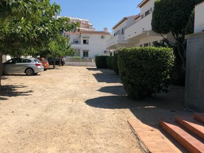 A parking area with cars, a gravel path, and buildings in the background.