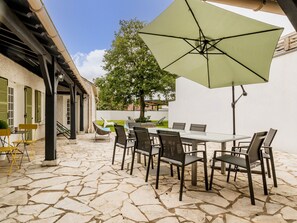 An outdoor patio with a stone floor, a table with chairs, and a large umbrella. - Charming Renovated House Near Nantes with Garden, Terrace, and Family Amenities (Le Bignon)
