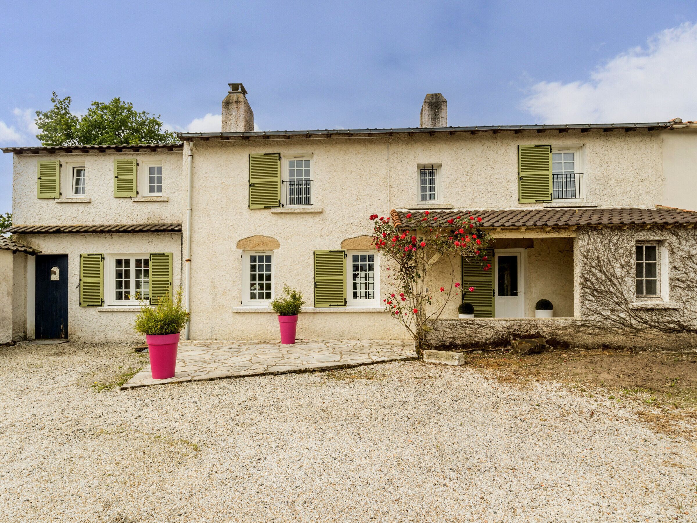 A two-story building with green shutters, a tiled roof, and a gravel courtyard.