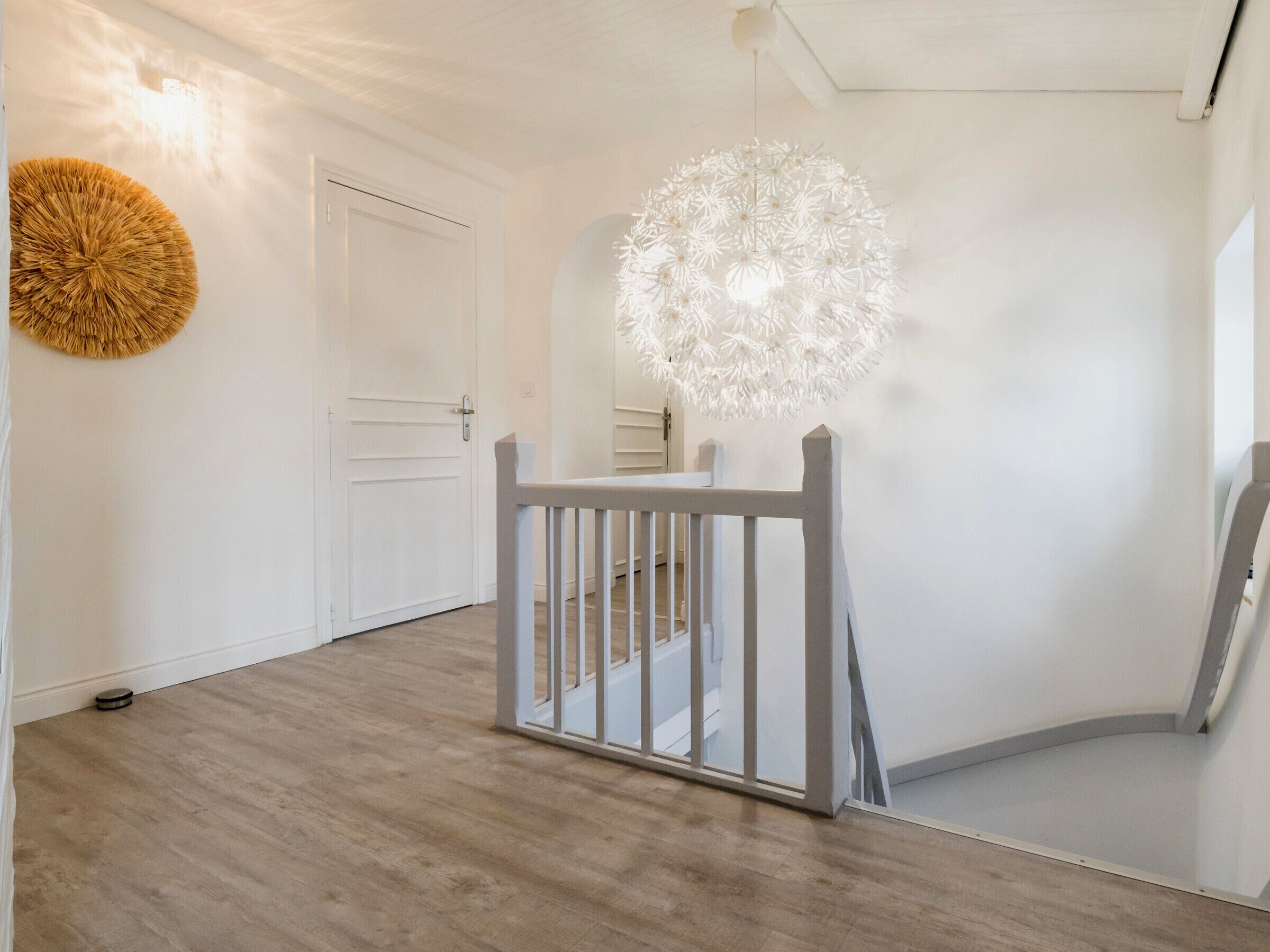Un intérieur moderne avec un plancher en bois, une porte blanche et un luminaire sphérique original.