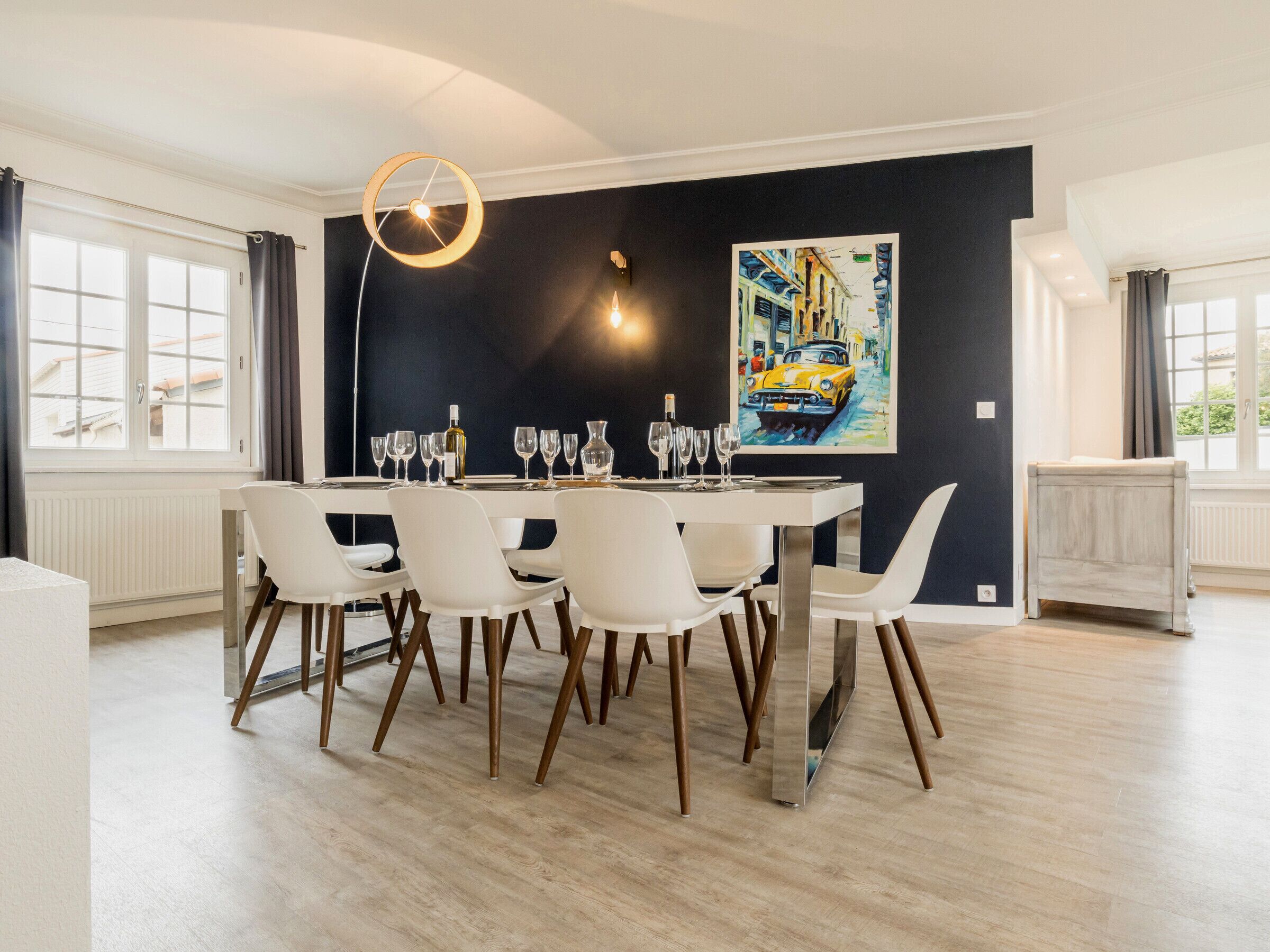A dining area with a round table, white chairs, and a painting on the wall.