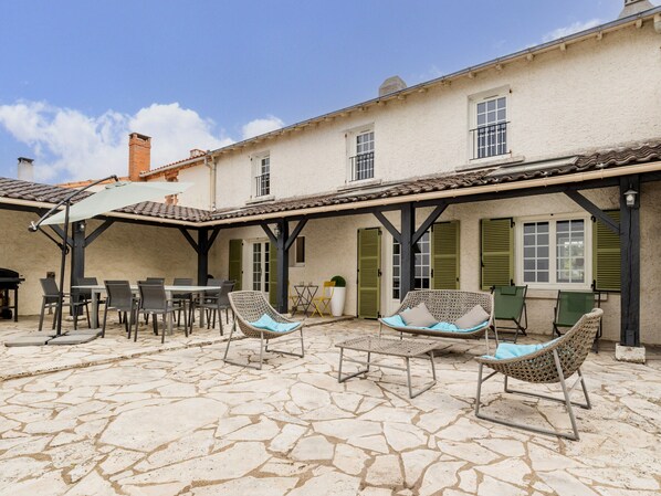 A courtyard with stone flooring, outdoor seating, and a building with green shutters. - Charming Renovated House Near Nantes with Garden, Terrace, and Family Amenities (Le Bignon)