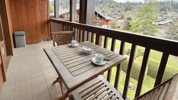 A wooden balcony with a table and chairs, overlooking a residential area with houses and trees. - Charming 2-BR + Cabin, Sleeps 6, Close to Jaillet Gondola and Sports Palace - Megève (Megève)