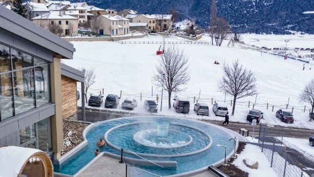 A spa area with a circular hot tub surrounded by snow-covered ground and parked cars.