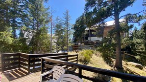 A wooden deck with two white chairs, surrounded by trees and a building in the background.