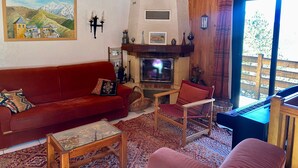 A cozy living room with a red sofa, a wooden chair, a fireplace, and a large window.