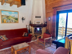 A cozy living room with a red sofa, a wooden chair, a fireplace, and a large window. - Chalet for 10 in Les Angles with pellet stove, parking and shuttle (Les Angles)