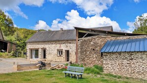 A stone building with a sloped roof, a bench, and a motorcycle in the foreground. - Comfortable country cottage - 6 guests (Mayenne)