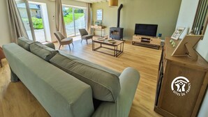 A spacious living room with a sofa, chairs, a coffee table, a TV, and a fireplace. - Comfortable country cottage - 6 guests (Mayenne)
