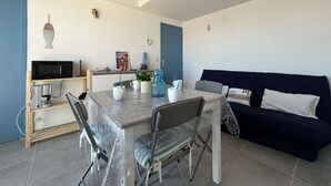 Ein kompakter Wohnbereich mit Esstisch, Stühlen, einer Couch, einer Mikrowelle, einer Kaffeemaschine und einer kleinen Küchenzeile.