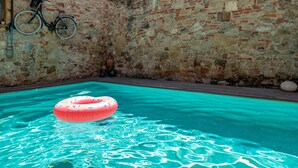Ein Swimmingpool mit klarem, blauem Wasser, einem rosa Schwimmreifen und einem Fahrrad, das an einer Steinmauer lehnt.