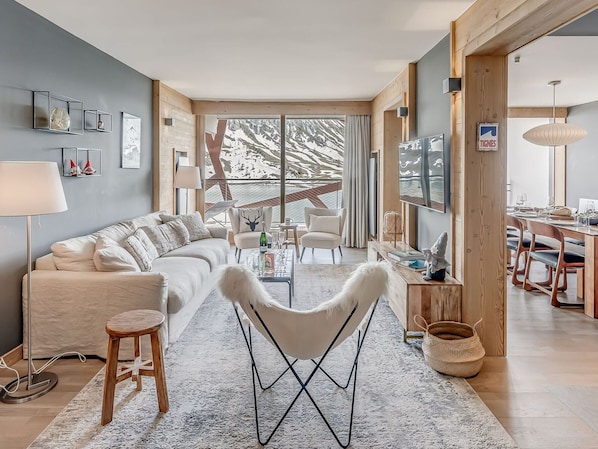 A modern living room with a sofa, armchairs, a coffee table, and a dining area with a table and chairs.