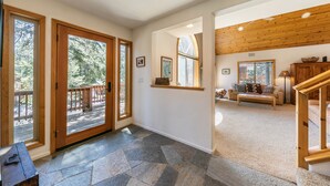 A spacious interior with a stone-tiled floor, wooden doors leading to a deck, and a cozy seating area with a sofa and coffee table. - Monthly Lease  - High Point By Tahoe Getaways with 3 Primary Suites! (Truckee)