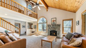 A spacious living room with a fireplace, leather sofas, a wooden coffee table, and a high ceiling with exposed beams. - Monthly Lease  - High Point By Tahoe Getaways with 3 Primary Suites! (Truckee)