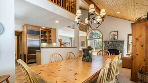 A spacious dining area with a wooden table and chairs, a stone fireplace, and a kitchen with a stainless steel refrigerator. - Monthly Lease  - High Point By Tahoe Getaways with 3 Primary Suites! (Truckee)