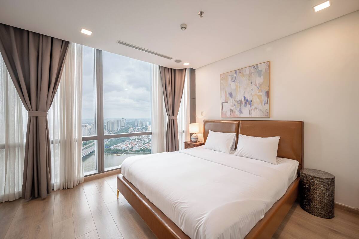 A modern hotel room with a large bed, a view of the city, and a painting on the wall.
