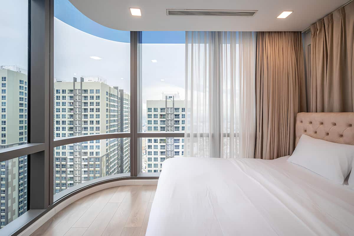 A modern hotel room with a large curved window, a tufted headboard, and a neatly made bed.