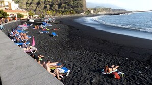 Une plage de sable noir, des gens qui prennent un bain de soleil et une montagne en arrière-plan.