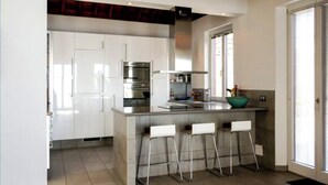 Une cuisine moderne avec des meubles blancs, des appareils en acier inoxydable et un îlot central doté de tabourets de bar.
