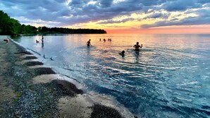 A beach scene with clear water, a sandy shore, and a sunset in the background. - Lakefront Oak Cottage • Hot Tub & Fire Pit (Sodus)