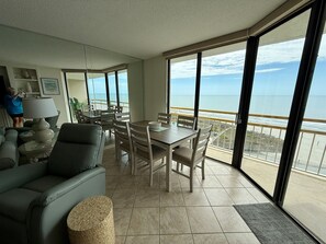 A living room with a dining area, large windows, and a view of the ocean.