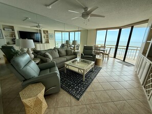 A spacious living room with a large sofa, a coffee table, and a view of the ocean through large windows.