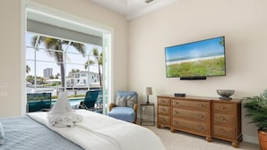 A bedroom with a large window, a bed, a dresser, a television, and a view of the outside. - Waterfront 4BR Marco Island home with heated pool, WiFi & kitchen. (Marco Island)