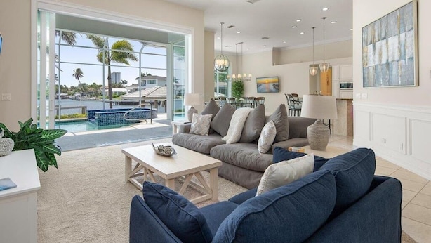A spacious living room with a large window, a pool view, and a kitchen area with modern appliances. - Waterfront 4BR Marco Island home with heated pool, WiFi & kitchen. (Marco Island)