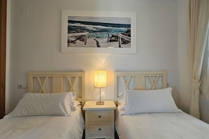 A hotel room with two beds, a nightstand with a lamp, and a framed picture of a beach scene on the wall.