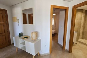 Un ba ño moderno con ducha, inodoro y zona de lavamanos con espejo y un mueble pequeño.