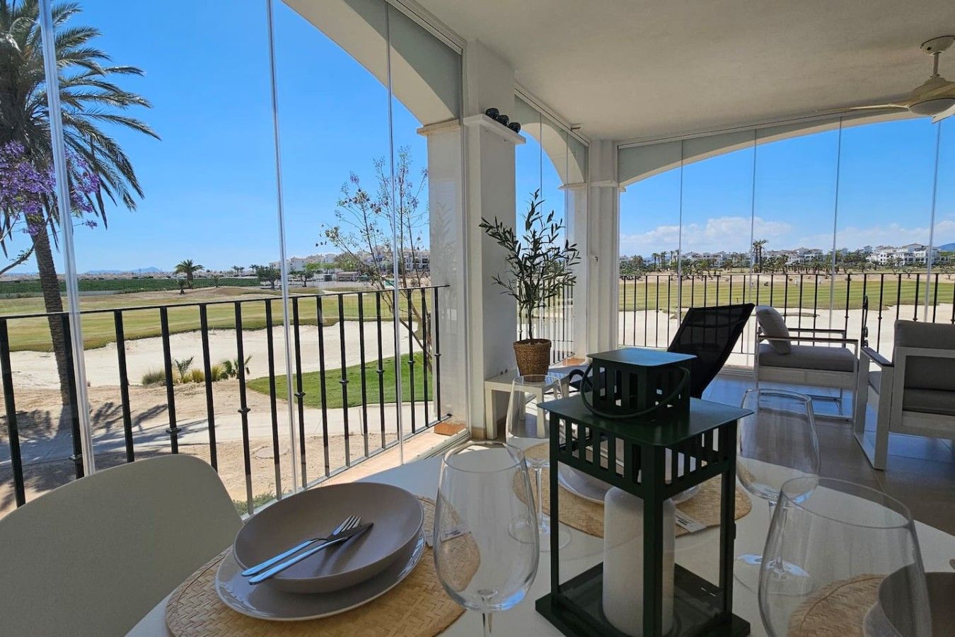 Un balcon ensoleillé avec une table à manger, des chaises et une vue sur un terrain de golf.