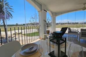 A sunlit balcony with a dining table, chairs, and a view of a golf course.