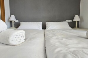 A hotel room with two beds, white linens, and bedside lamps.