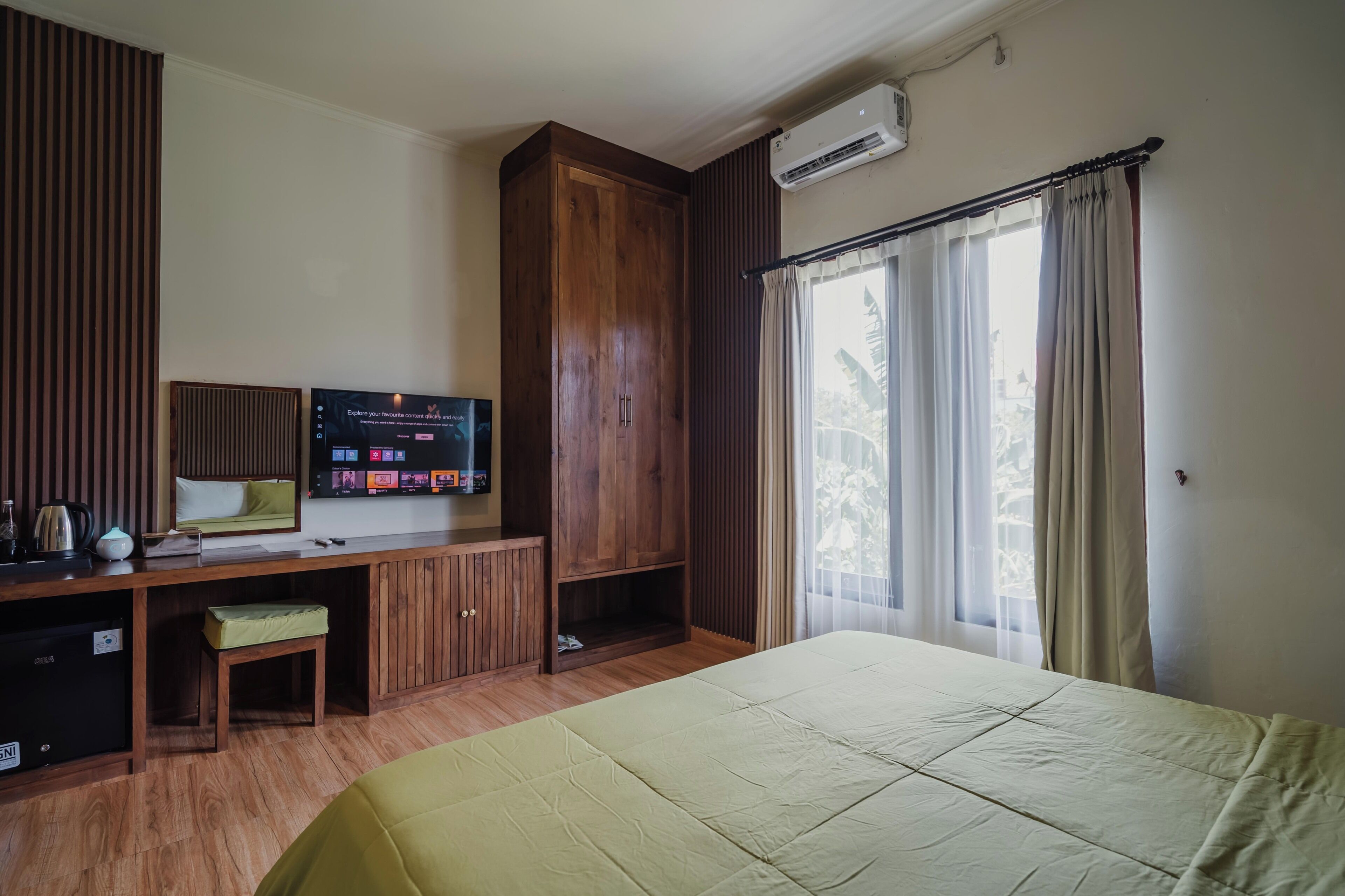 A hotel room with a bed, a desk with a television, a wardrobe, and a window with curtains.
