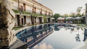 A modern hotel with a pool, outdoor seating, and a statue. - You Suite Seminyak (Legian)